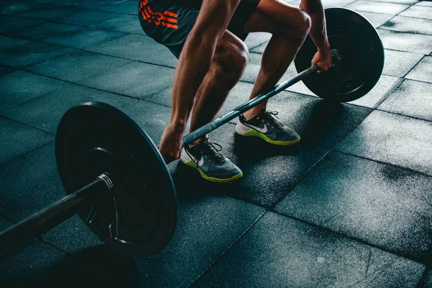 Foto ilustrativa de treino de força com barra em uma academia, por Unsplash